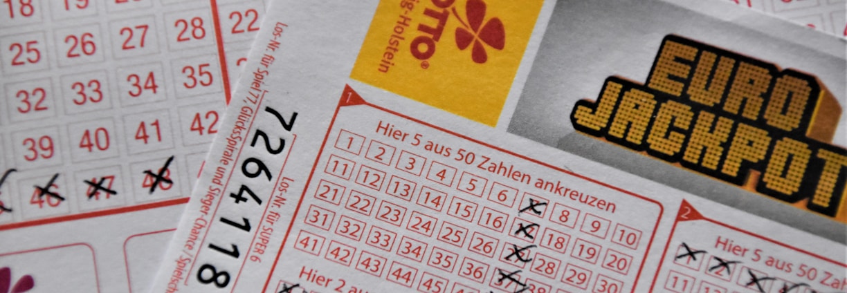 A close-up image of lottery tickets featuring crossed-out numbers, brand logos, and various numbers in a grid format. The tickets have sections for different games, and numbers are marked with black crosses.